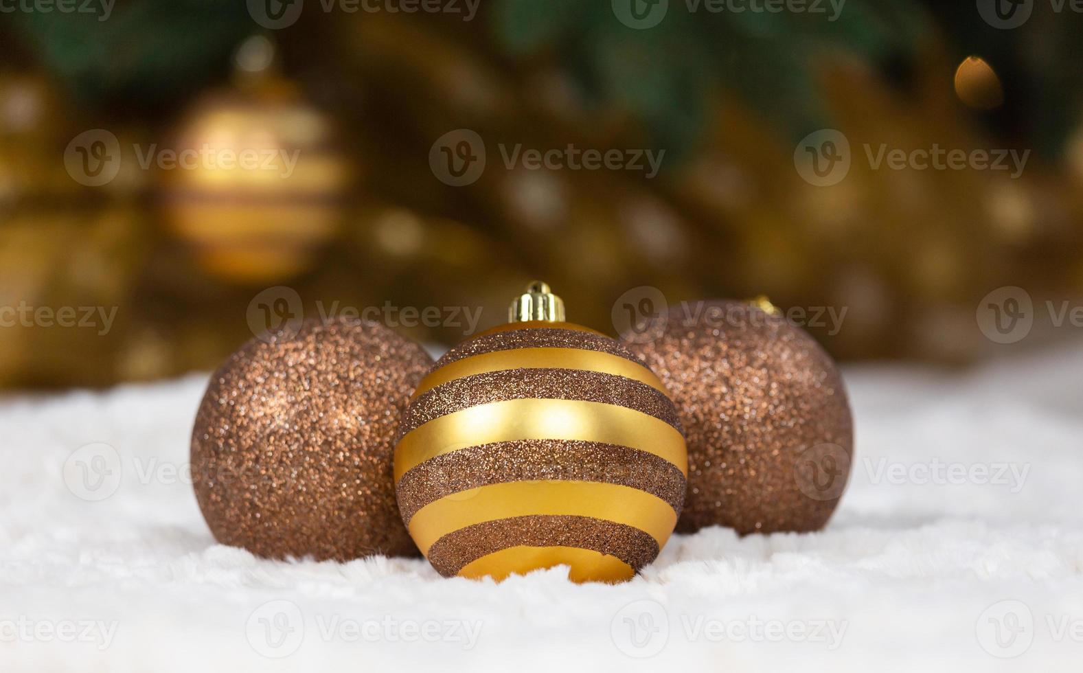 Tres bolas de oro de Navidad yacen sobre un plaid blanco con el telón de fondo de un árbol de Navidad y una guirnalda brillante foto