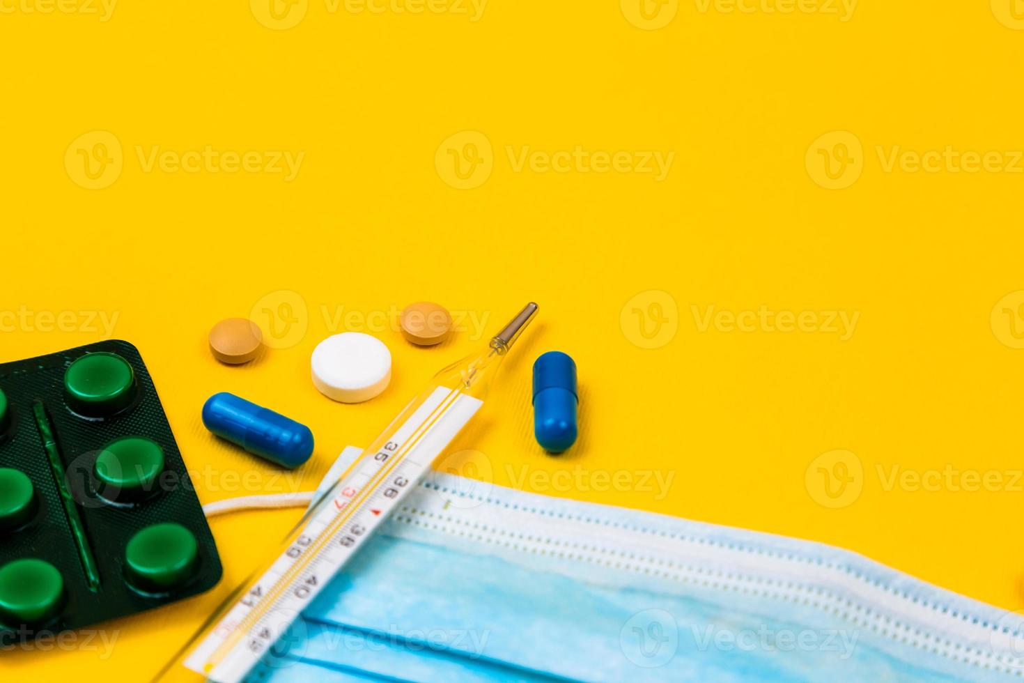 Protective medical mask on yellow background surrounded with colorful pills photo