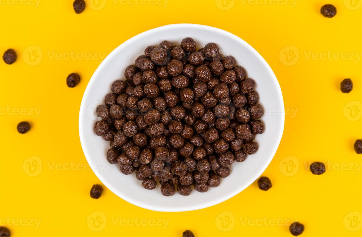 Recipiente blanco con bolas de cereal de maíz de chocolate y leche sobre fondo amarillo foto