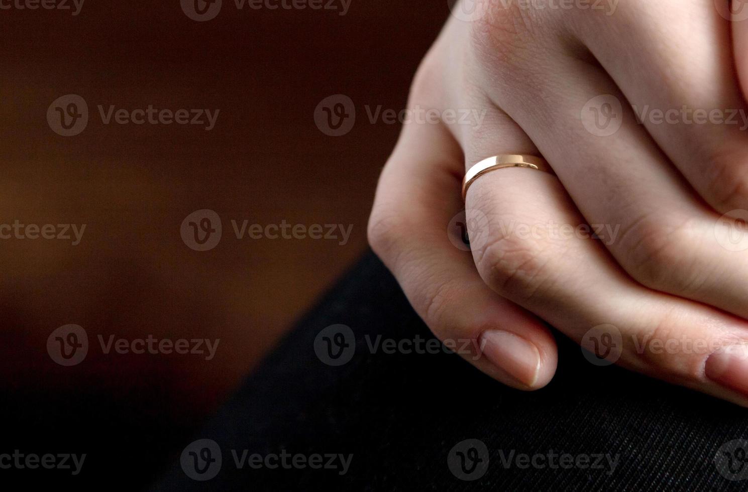 Primer plano de la mano de una persona con un anillo de bodas sobre una superficie marrón foto