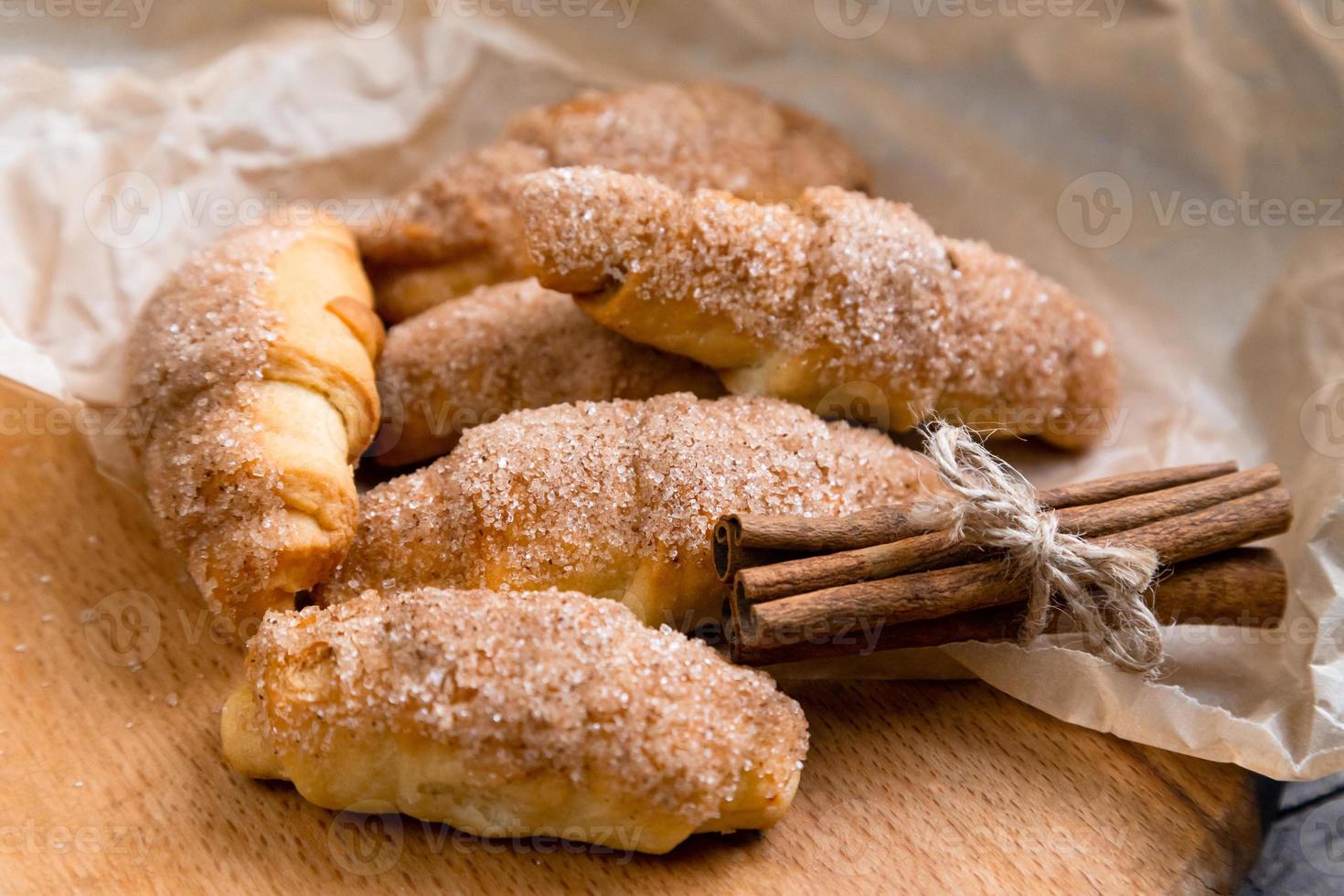 Fresh croissants with cinnamon on wrinkled paper on wooden background table photo