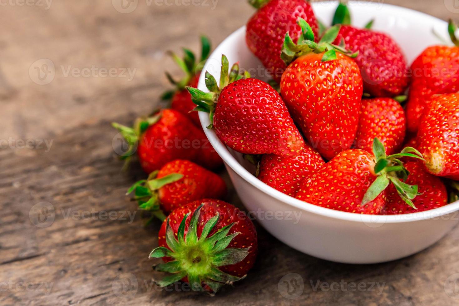 Recipiente lleno de fresas frescas sobre una mesa marrón foto