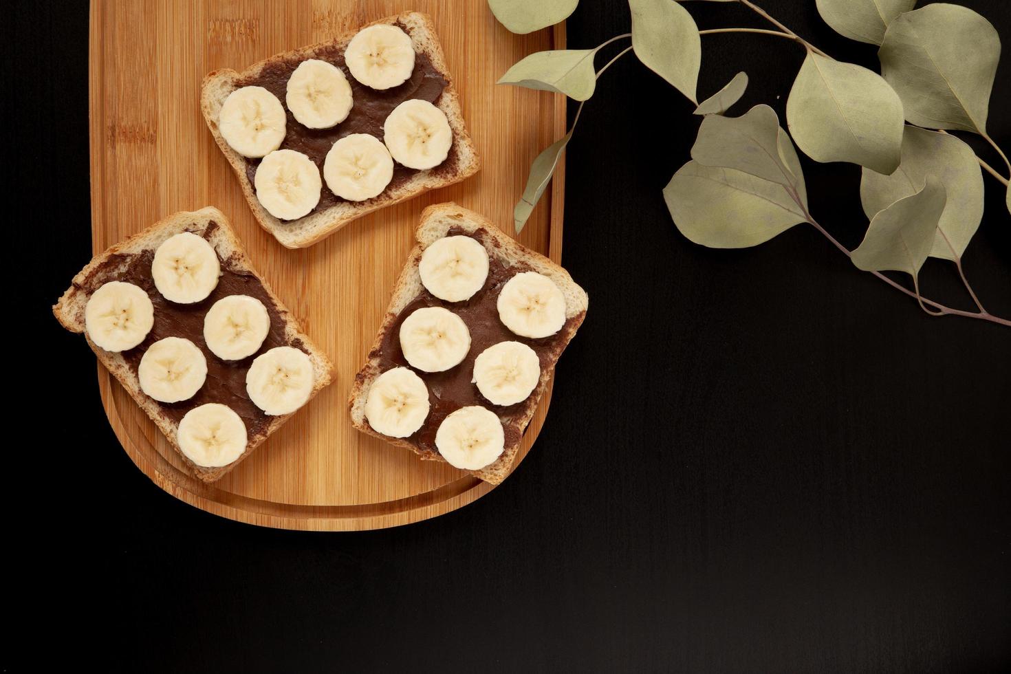 Tres tostadas de pan blanco de plátano untadas con mantequilla de chocolate sobre una tabla de cortar sobre un fondo oscuro foto