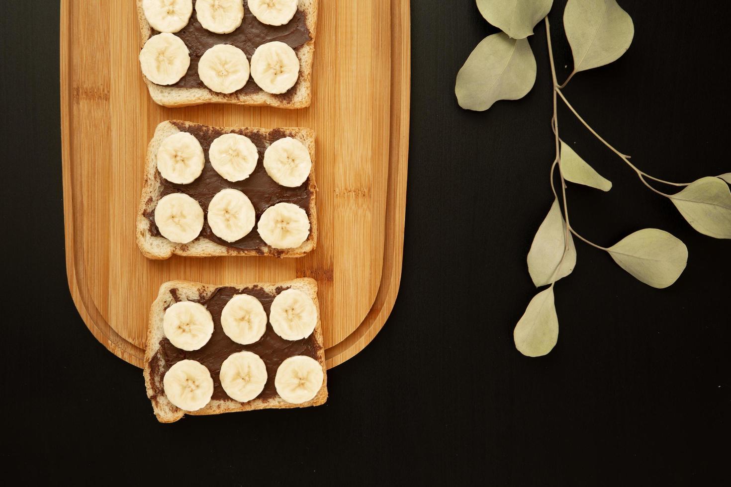 Tres tostadas de pan blanco de plátano untadas con mantequilla de chocolate sobre una tabla de cortar sobre un fondo oscuro foto