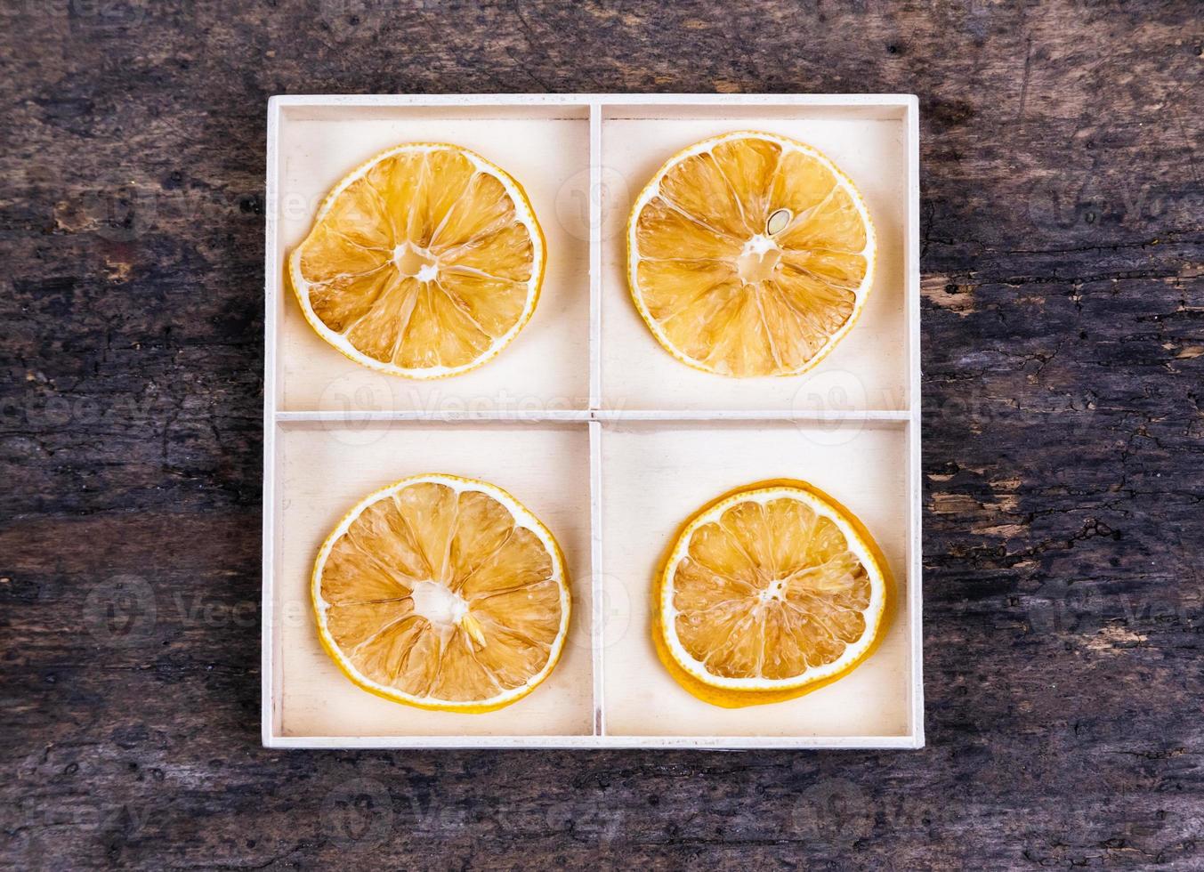 una caja blanca con compartimentos sobre un fondo de madera lleno de naranjas secas foto