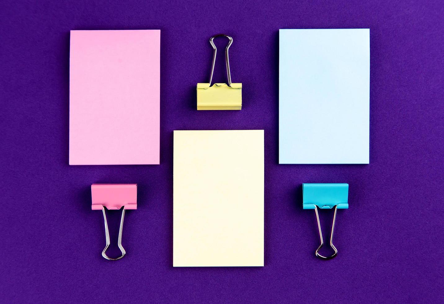Bloc de notas con un juego de clips de papel de colores sobre fondo púrpura foto