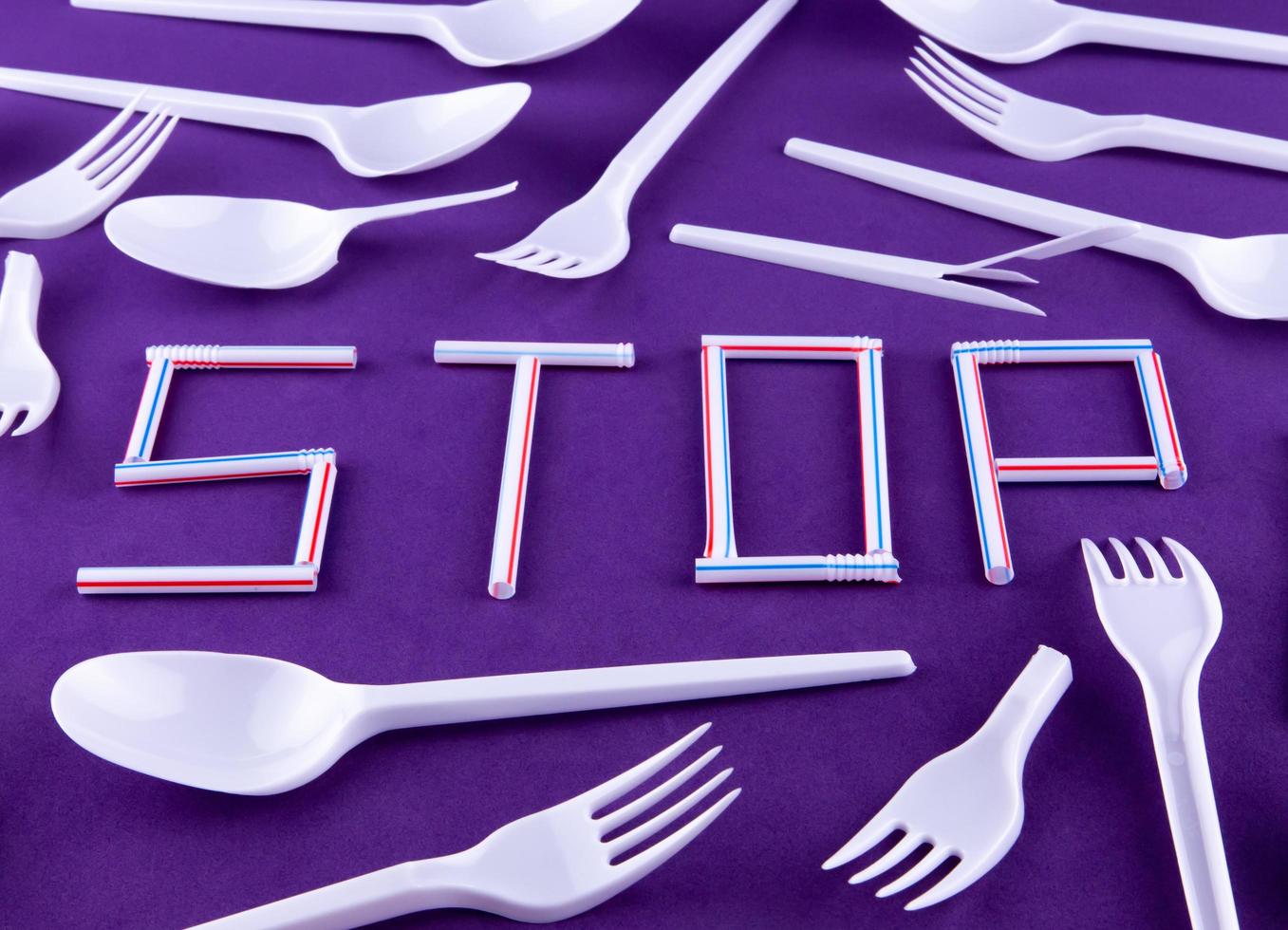 The word stop made of plastic tubes on a purple background with plastic utensils photo