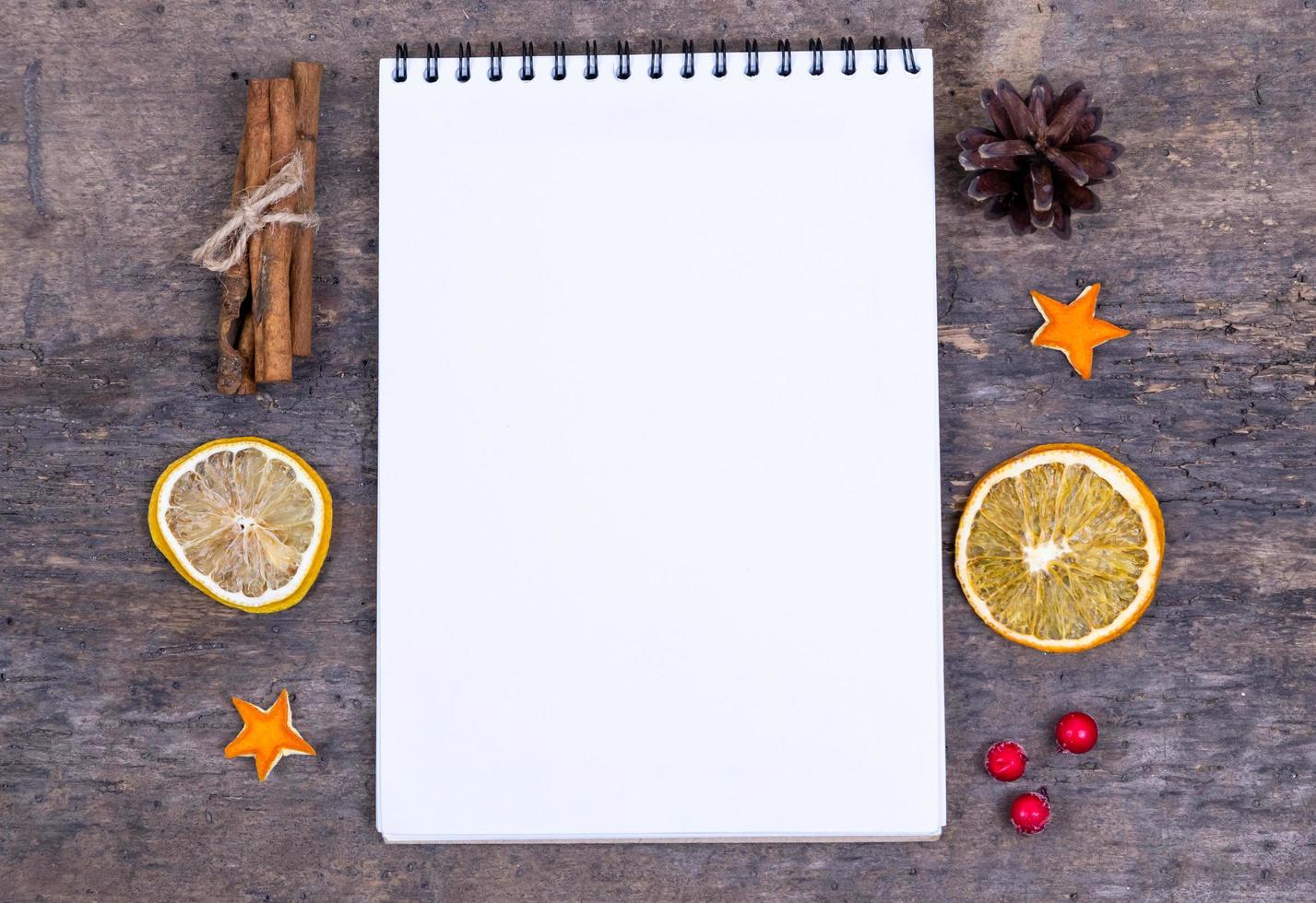 A pile of cinnamon sticks dried orange and tangerine stars on old wooden table with white empty piece of paper photo