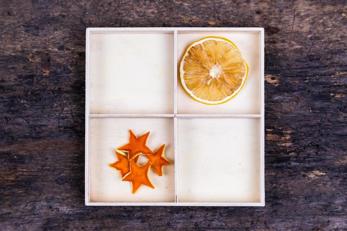 A white box with compartments on a wooden background filled with dried oranges and tangerine stars photo