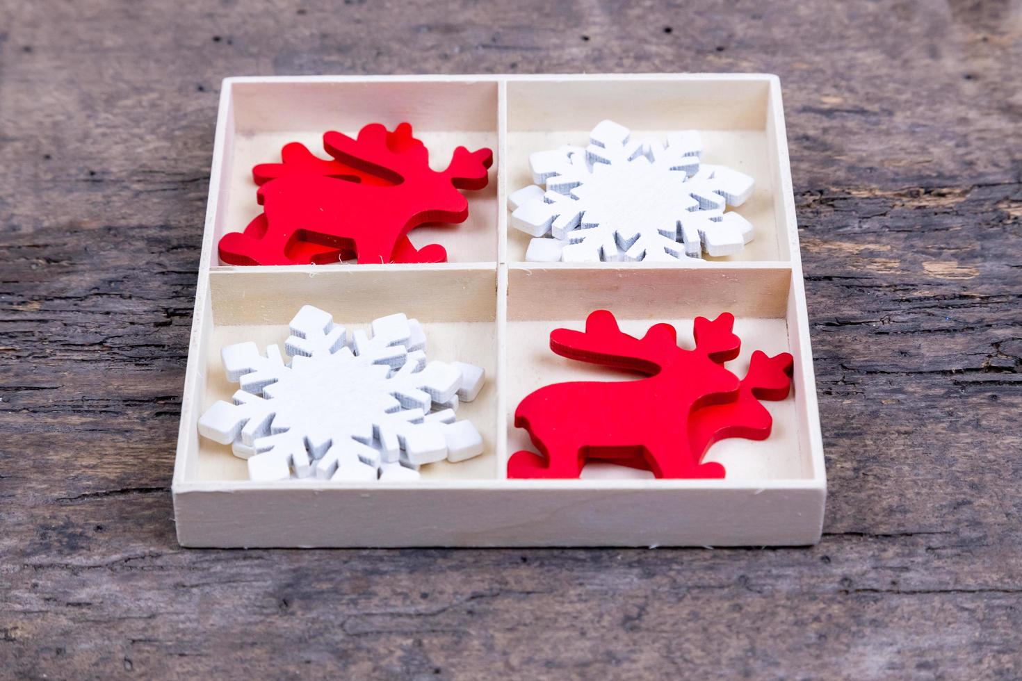 A white box with compartments on a wooden background filled with Christmas deer and snowflakes photo