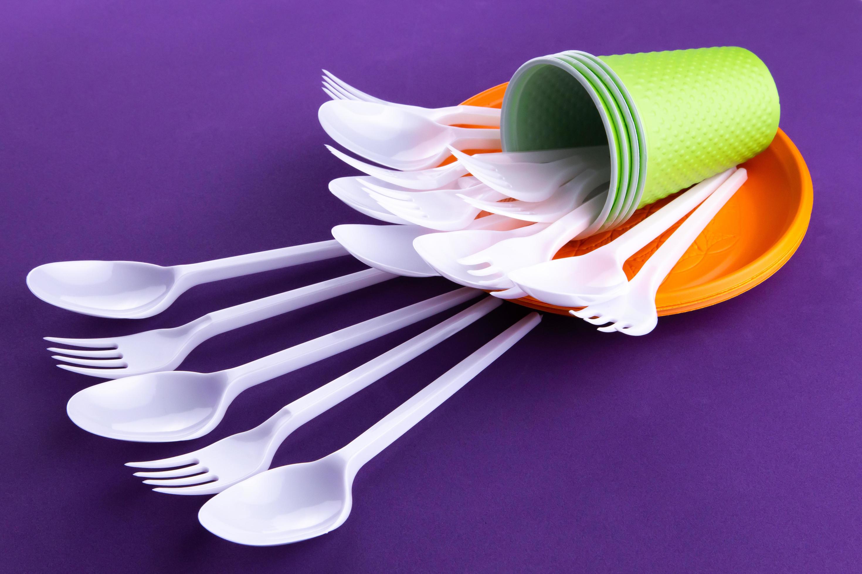Bright orange and green set of disposable plastic tableware on purple