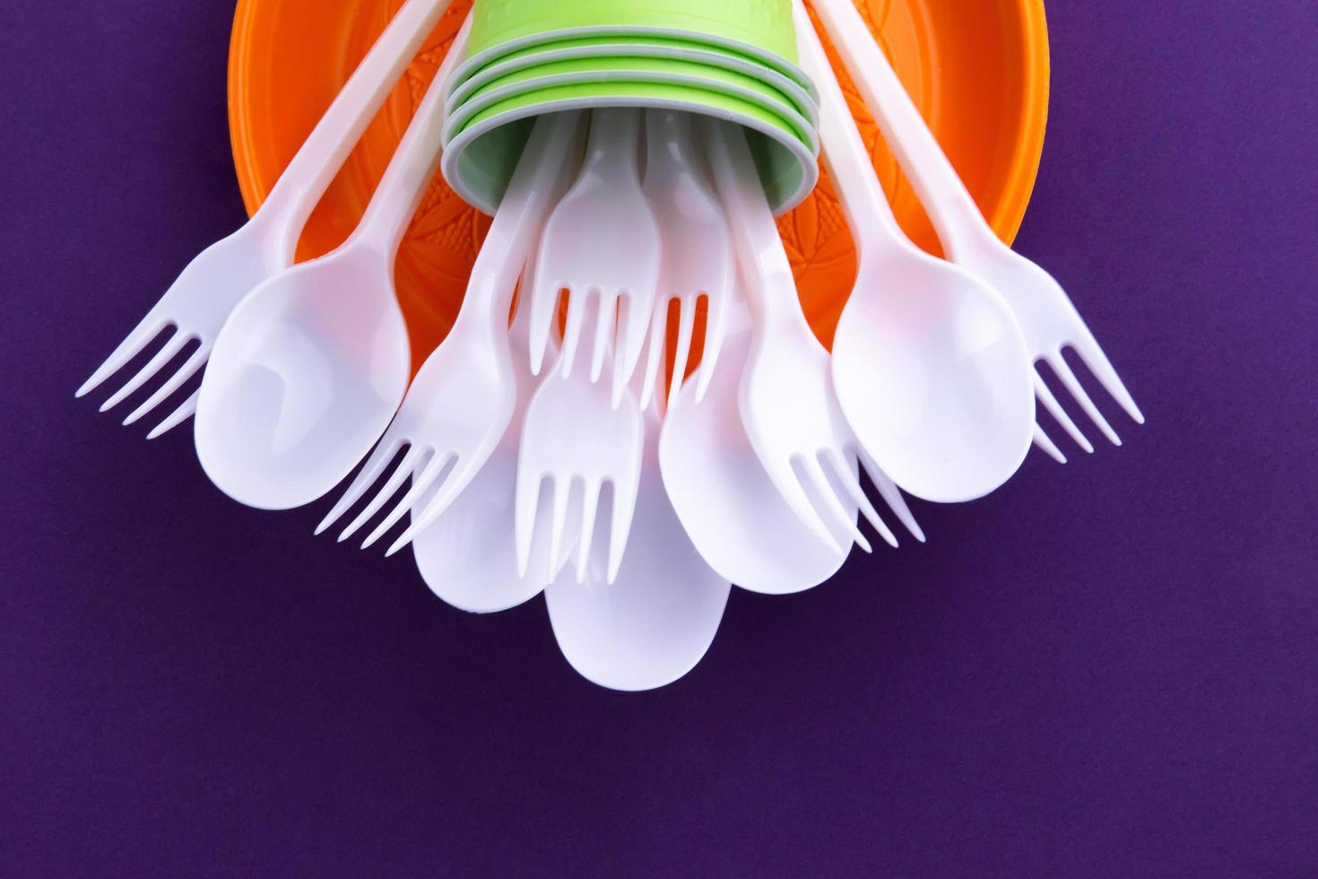 Bright orange and green set of disposable plastic tableware on purple background photo