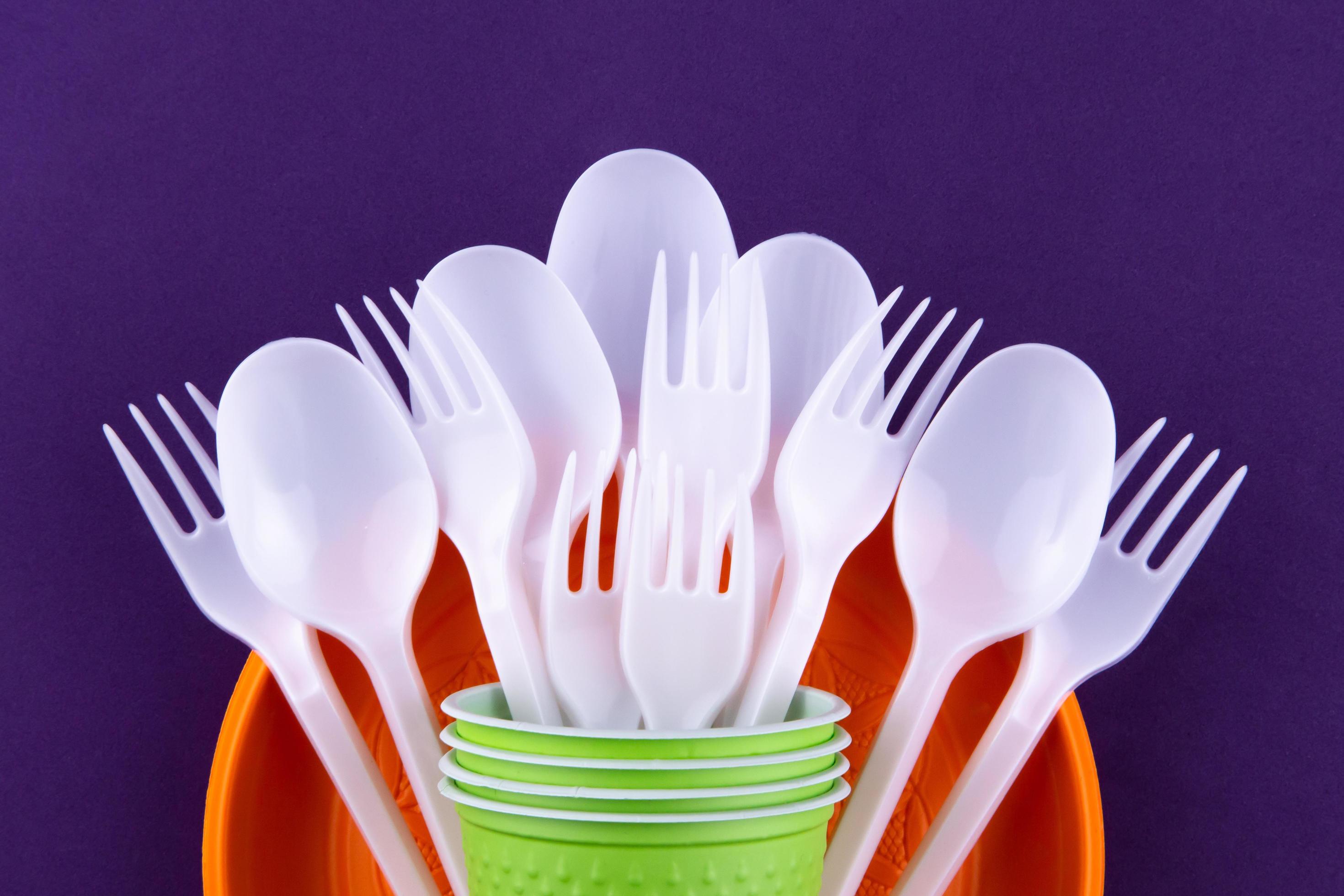 Bright orange and green set of disposable plastic tableware on purple