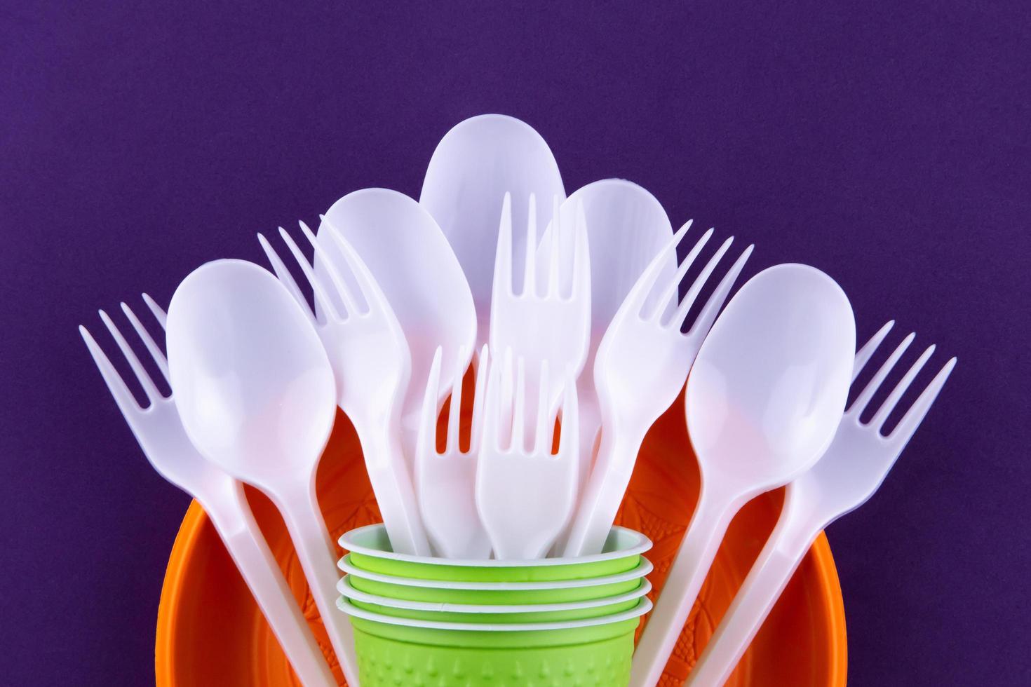 Bright orange and green set of disposable plastic tableware on purple background photo