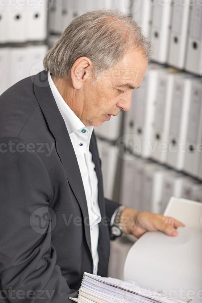 Middle aged man with white shirt is standing in front of a shelf wall with documents photo