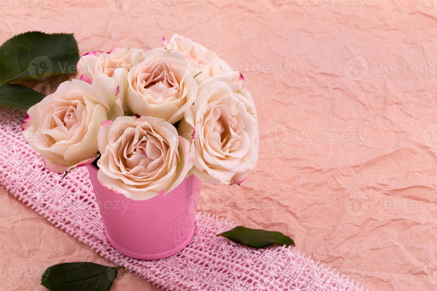 A bouquet of beautiful roses stands in a small bucket on a lace ribbon photo