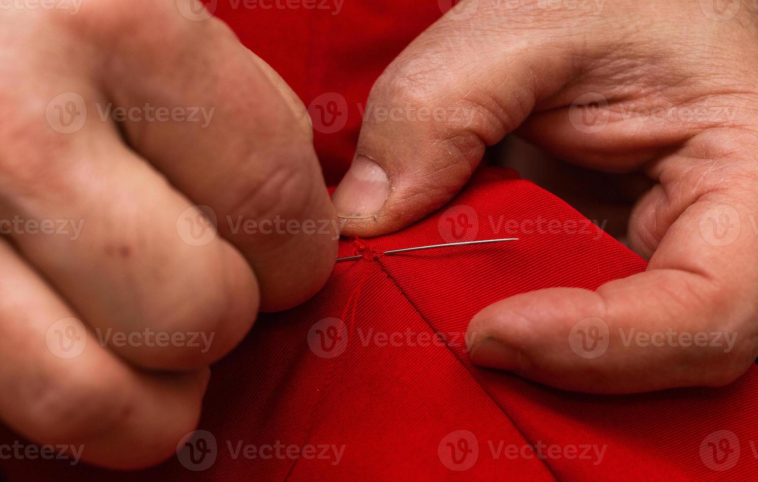 Las manos cosen con aguja e hilo en casa. foto