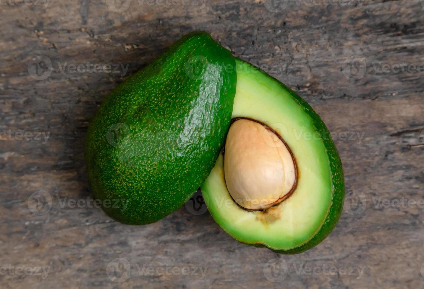 Aguacate fresco cortado por la mitad sobre fondo de tablero de madera foto