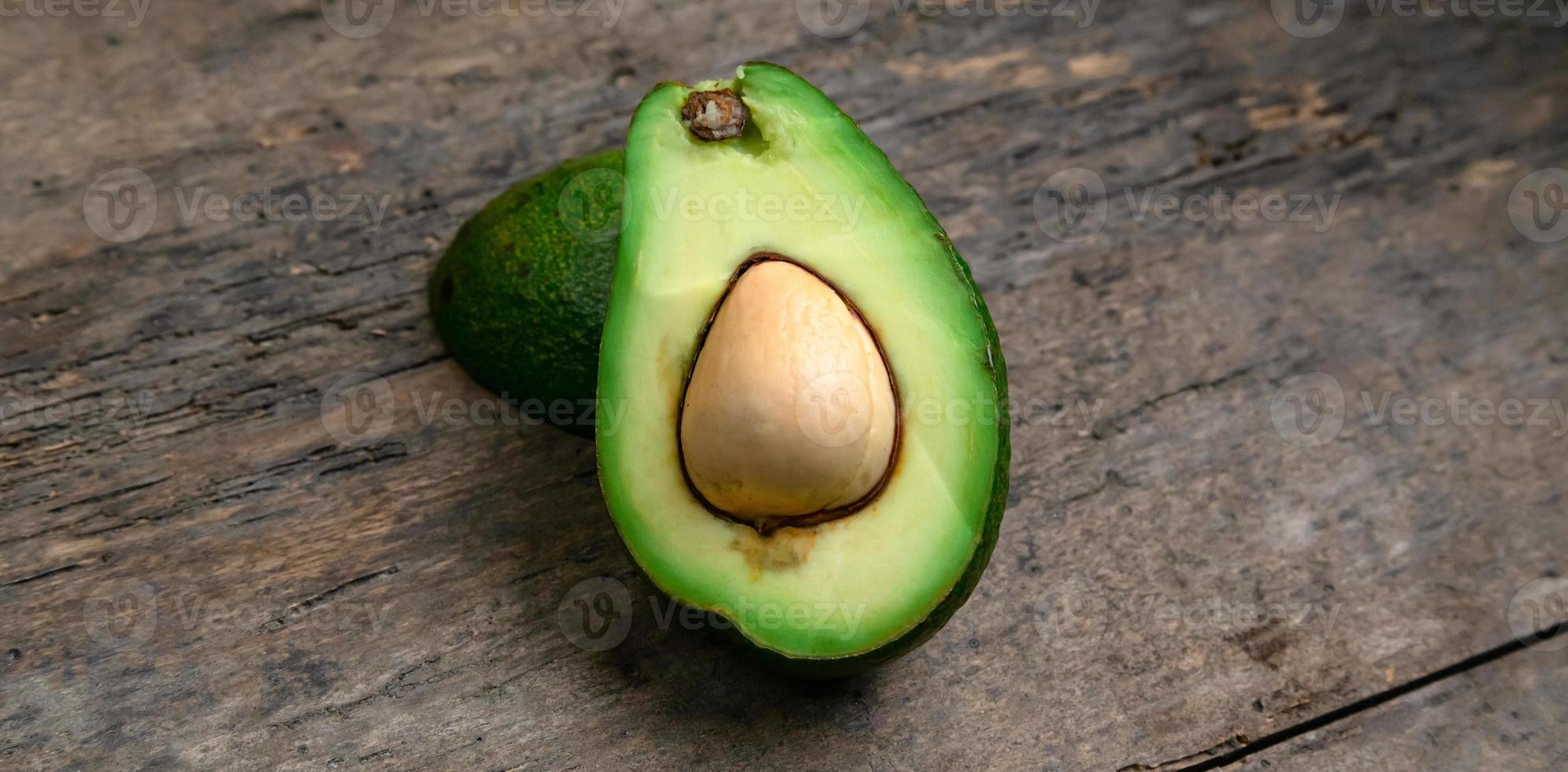 Aguacate fresco cortado por la mitad sobre fondo de tablero de madera foto