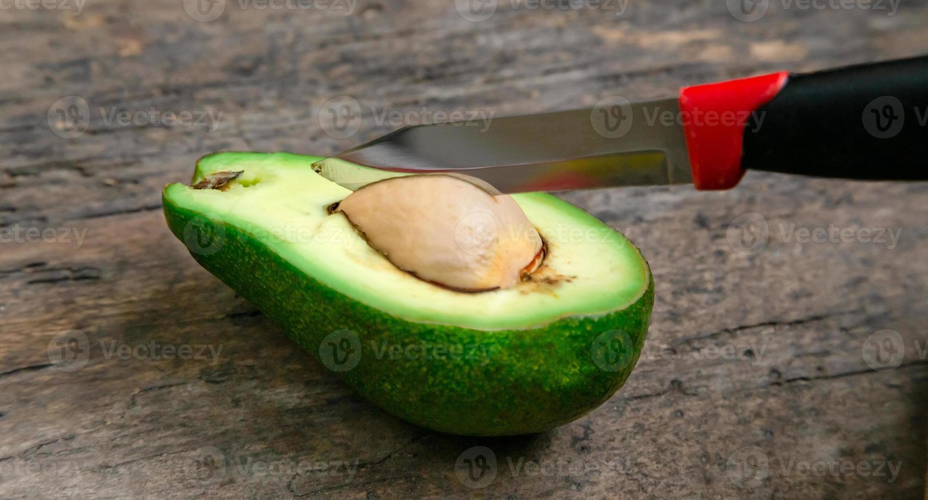 Aguacate fresco cortado por la mitad sobre una tabla de madera con fondo de cuchillo foto