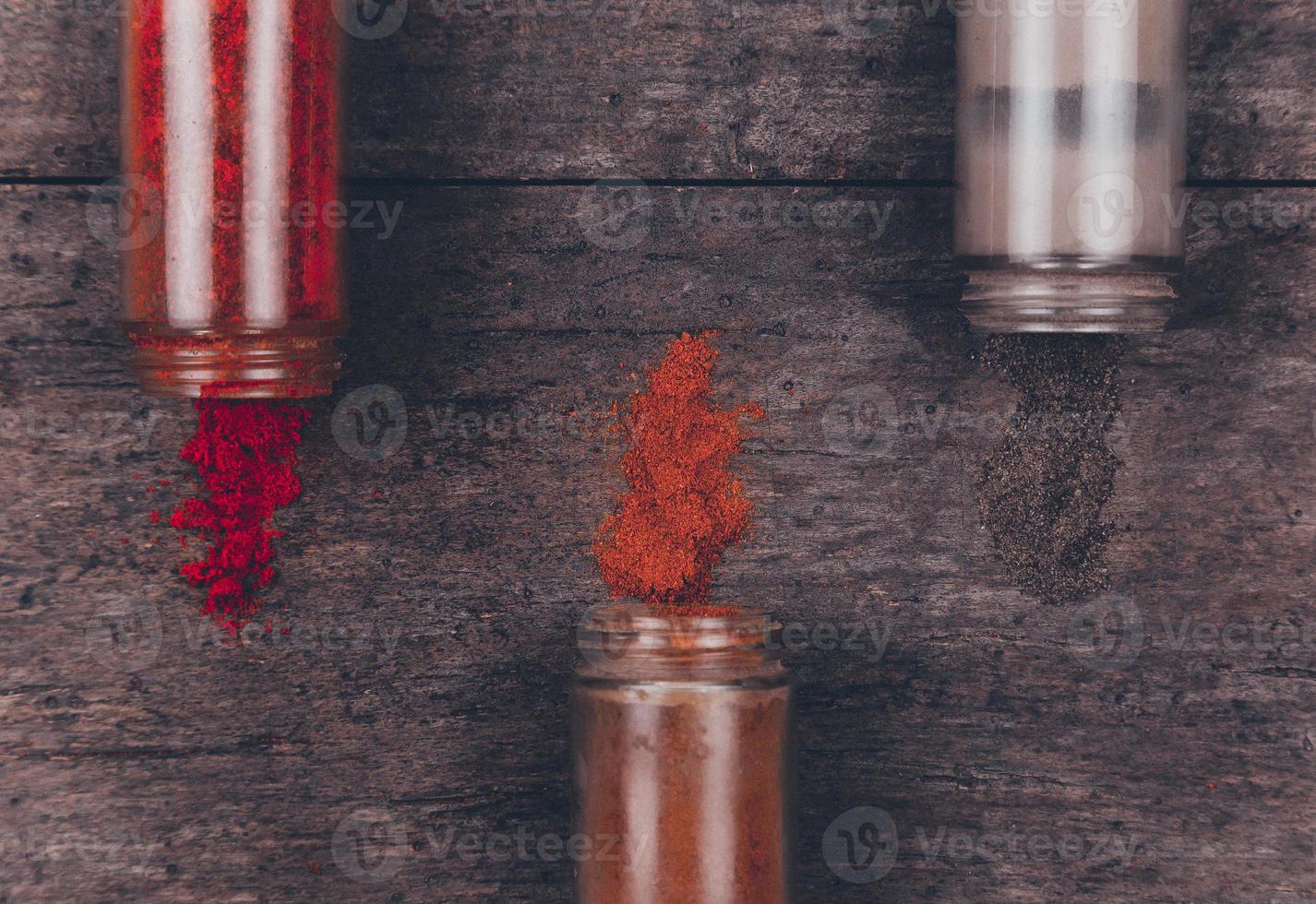 Chilli colorful powder spices scattered from bottle on wooden background photo