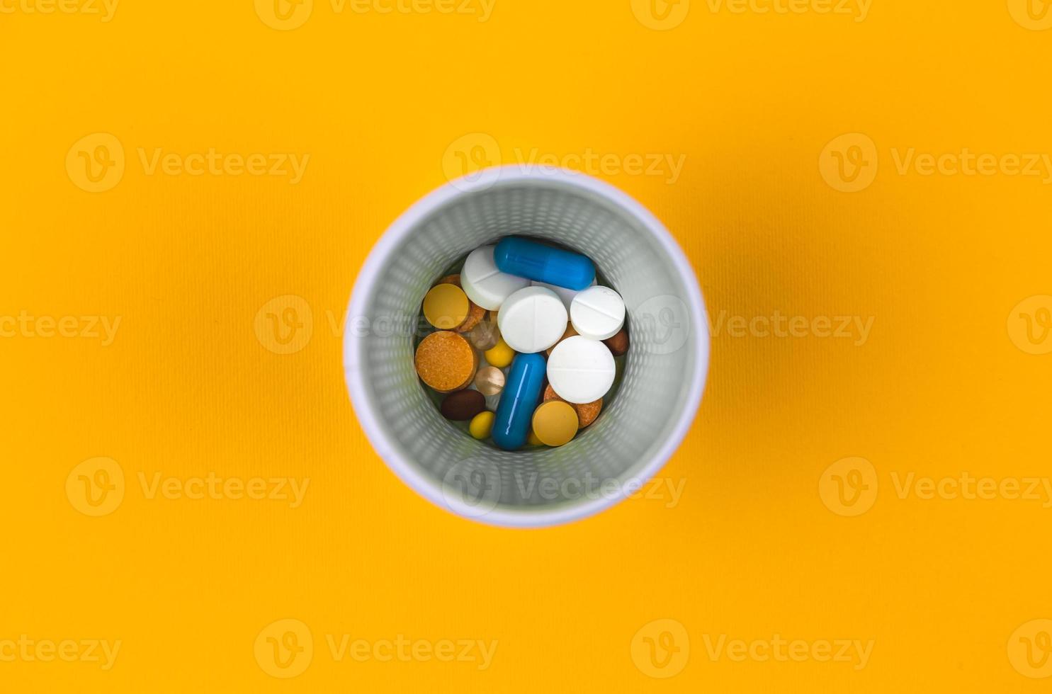 Colorful pills or tablets in glass on yellow background photo