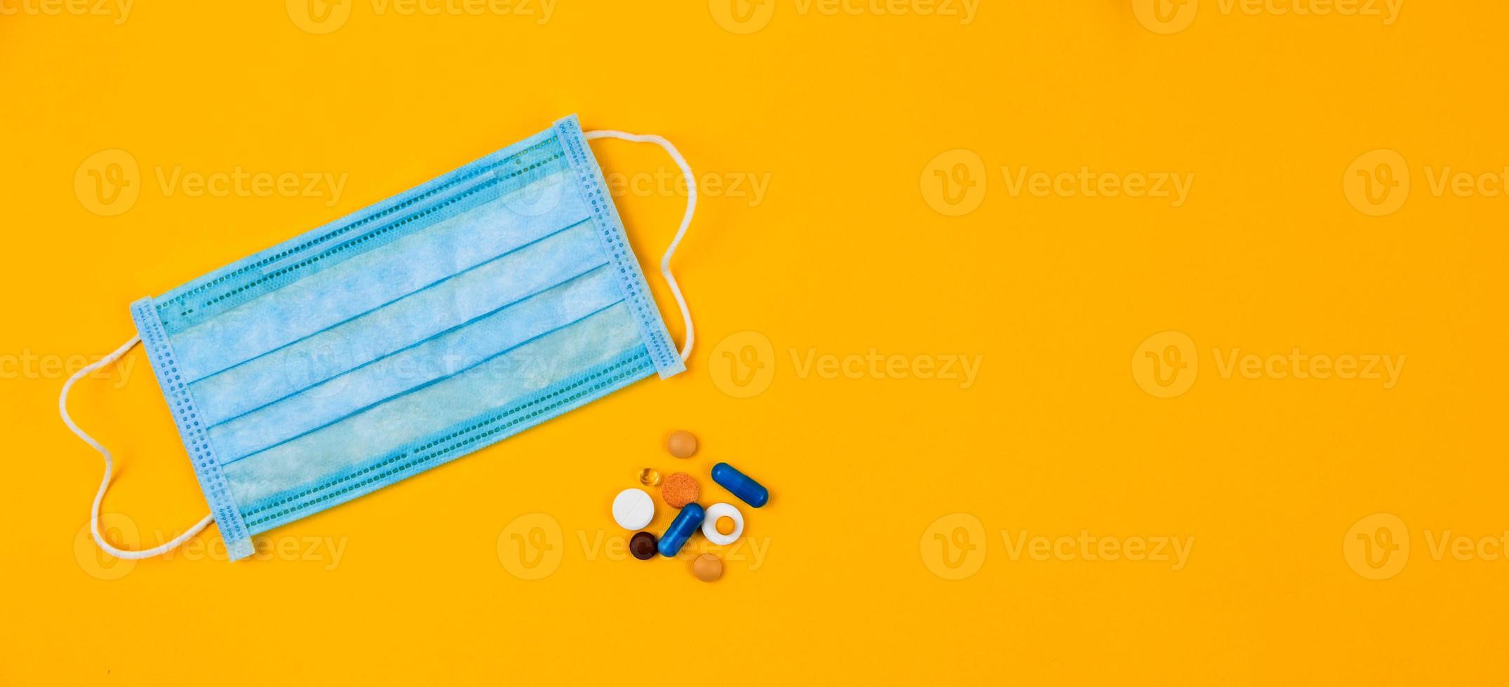 Blue protective medical mask on yellow background surrounded with colorful pills photo