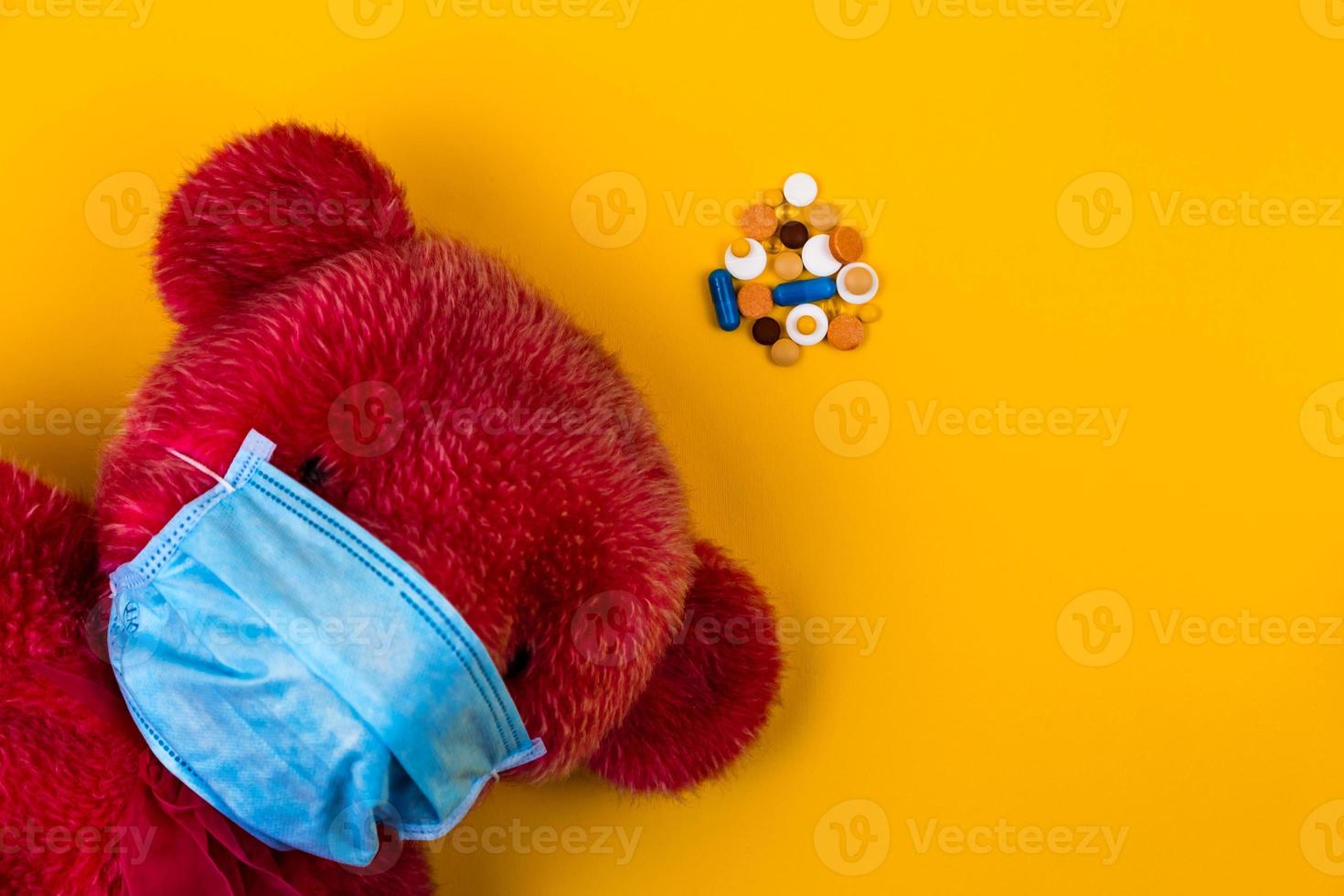 Oso de peluche rojo solitario en una máscara médica protectora sobre un fondo amarillo foto