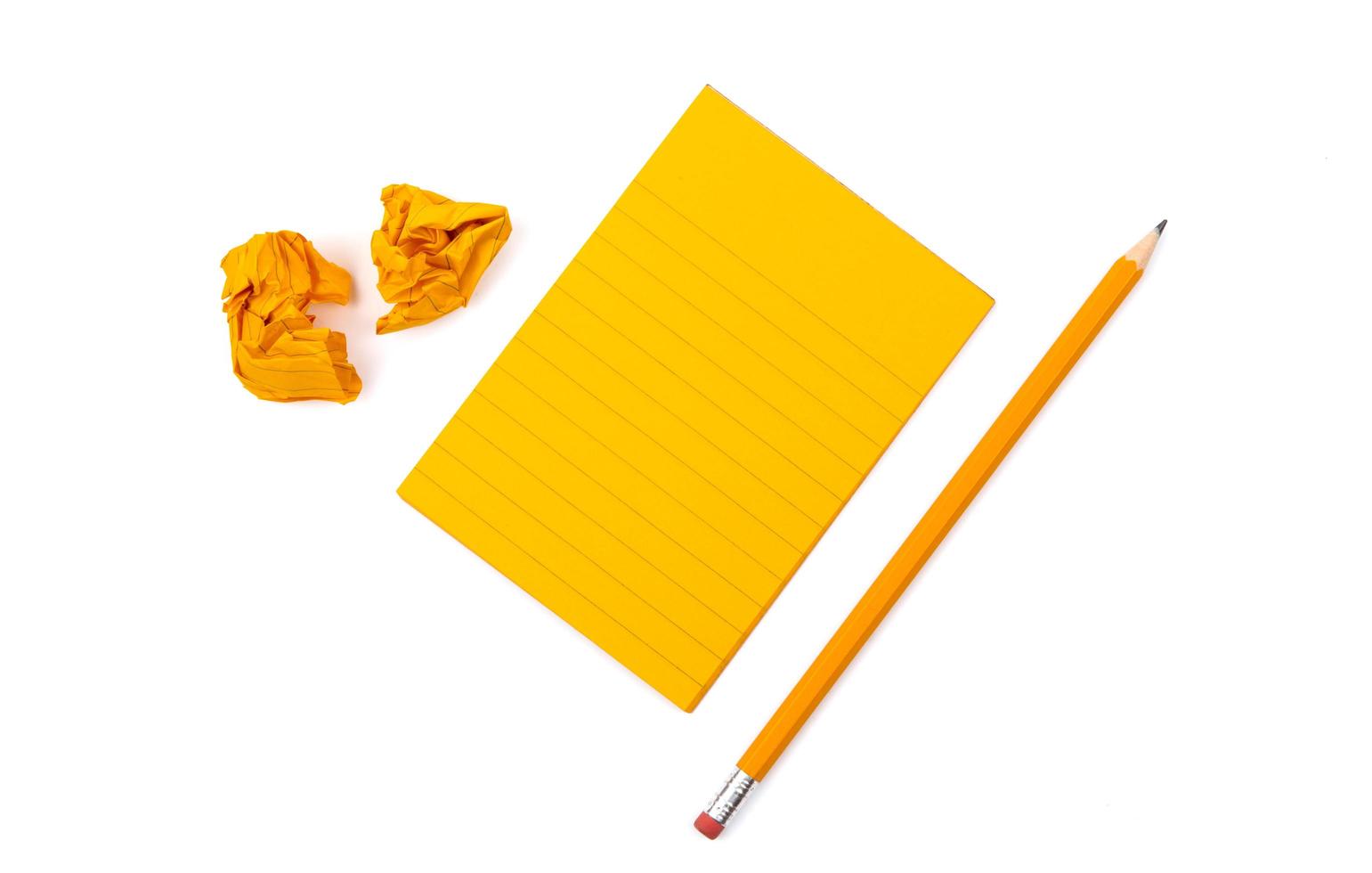 A striped notebook with orange sheets next to a sharpened pencil and two crumpled pieces of paper photo