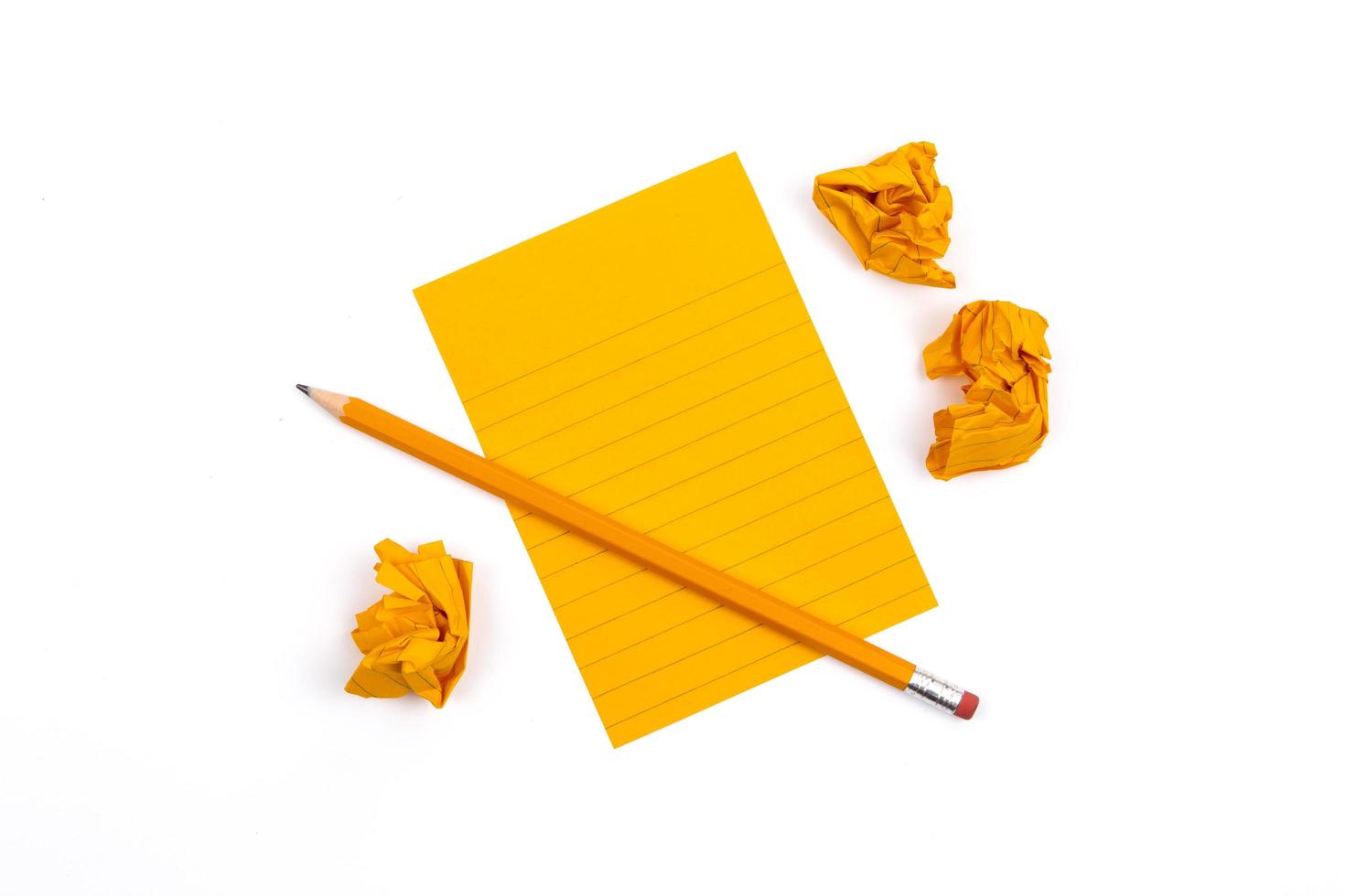 A striped notebook with orange sheets next to a sharpened pencil and three crumpled pieces of paper photo