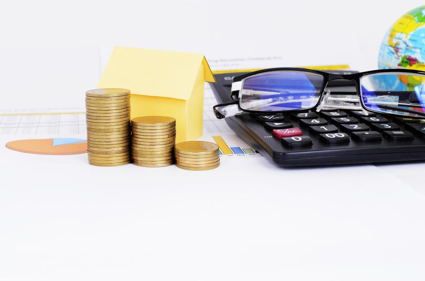 Mortgageloans concept with coins stack and yellow paper house and Eyeglasses and calculator on business chart document photo