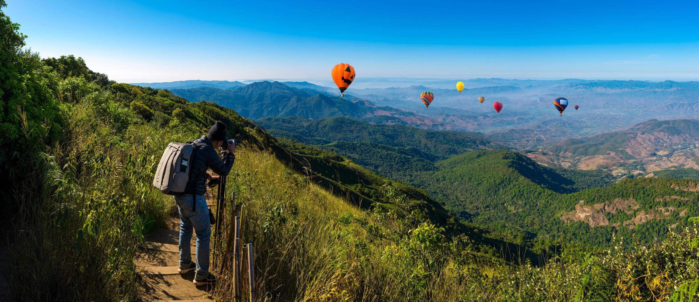 Professional photographer takes landscape photos on a mountain with hot air balloons in the background