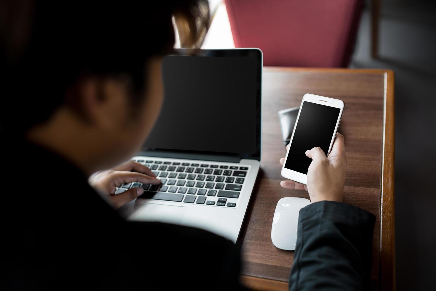 Cerca del empresario sosteniendo un teléfono inteligente y usando una computadora portátil mientras se conecta a internet inalámbrico foto