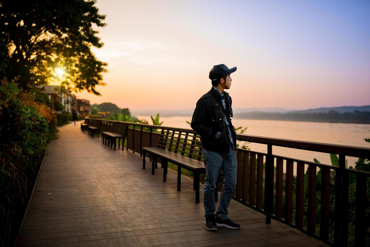 Traveler walking over a wooden bridge near the river in sunset photo