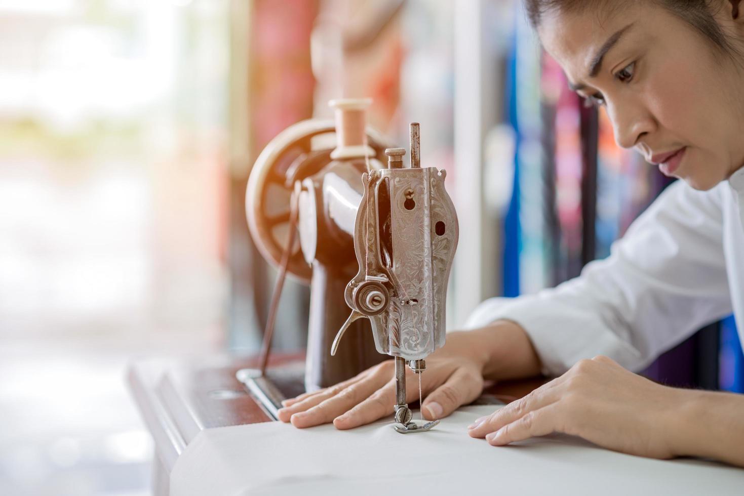 La mujer está cosiendo con una máquina de coser en casa mientras está sentada en su lugar de trabajo foto