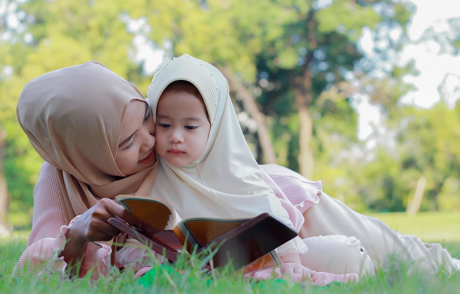 Madre musulmana enseña a su hija a leer felizmente el Corán en el parque en verano. foto