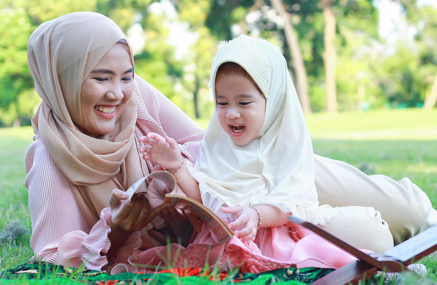 Muslim mother teaches her daughter to happily read the Quran in the park in the summer photo