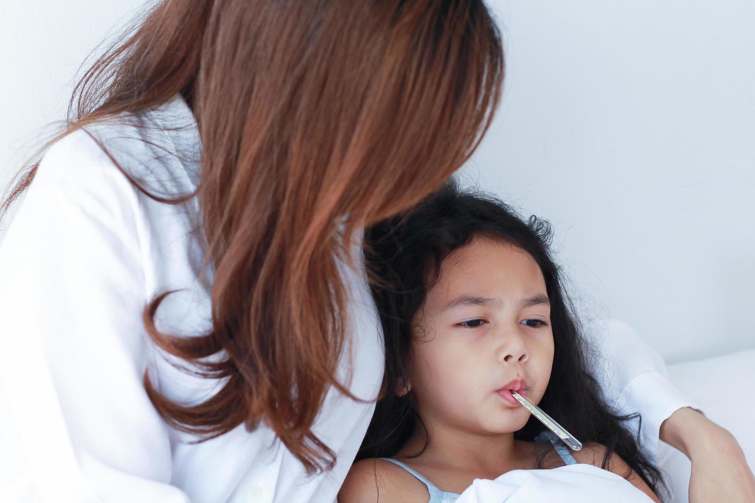 madre asiática midiendo la temperatura de su hija foto