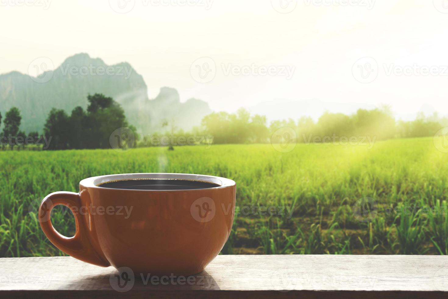 Café caliente negro caliente con humo sobre una mesa de madera con un paisaje de la naturaleza con la montaña en el tiempo de la mañana foto