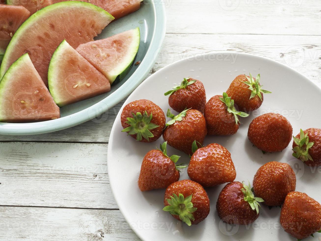 Red ripe strawberries on a white plate and fresh watermelon slices on a green plate top view photo