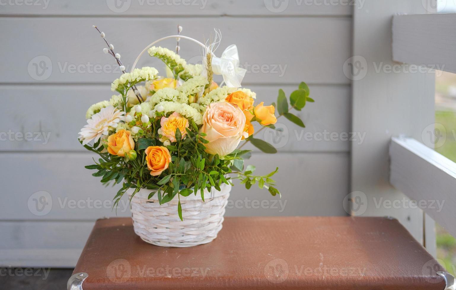 a beautiful bouquet of fresh flowers in a basket on a vintage suitcase on a gray wall background photo