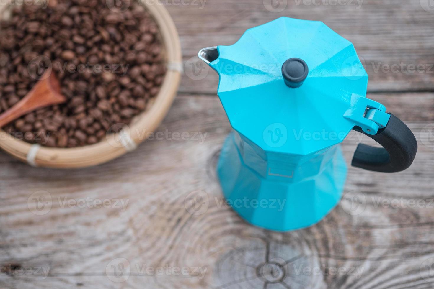 Cafetera de géiser azul y granos de café tostados en el fondo de una vieja placa de madera foto