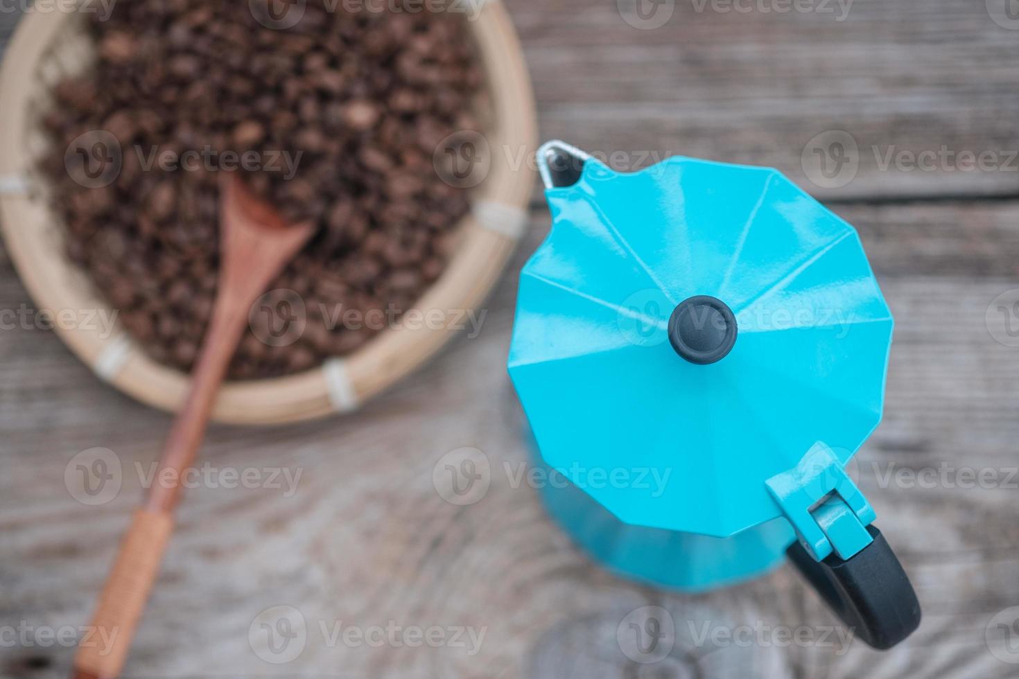 Cafetera de géiser azul y granos de café tostados en el fondo de una vieja placa de madera foto