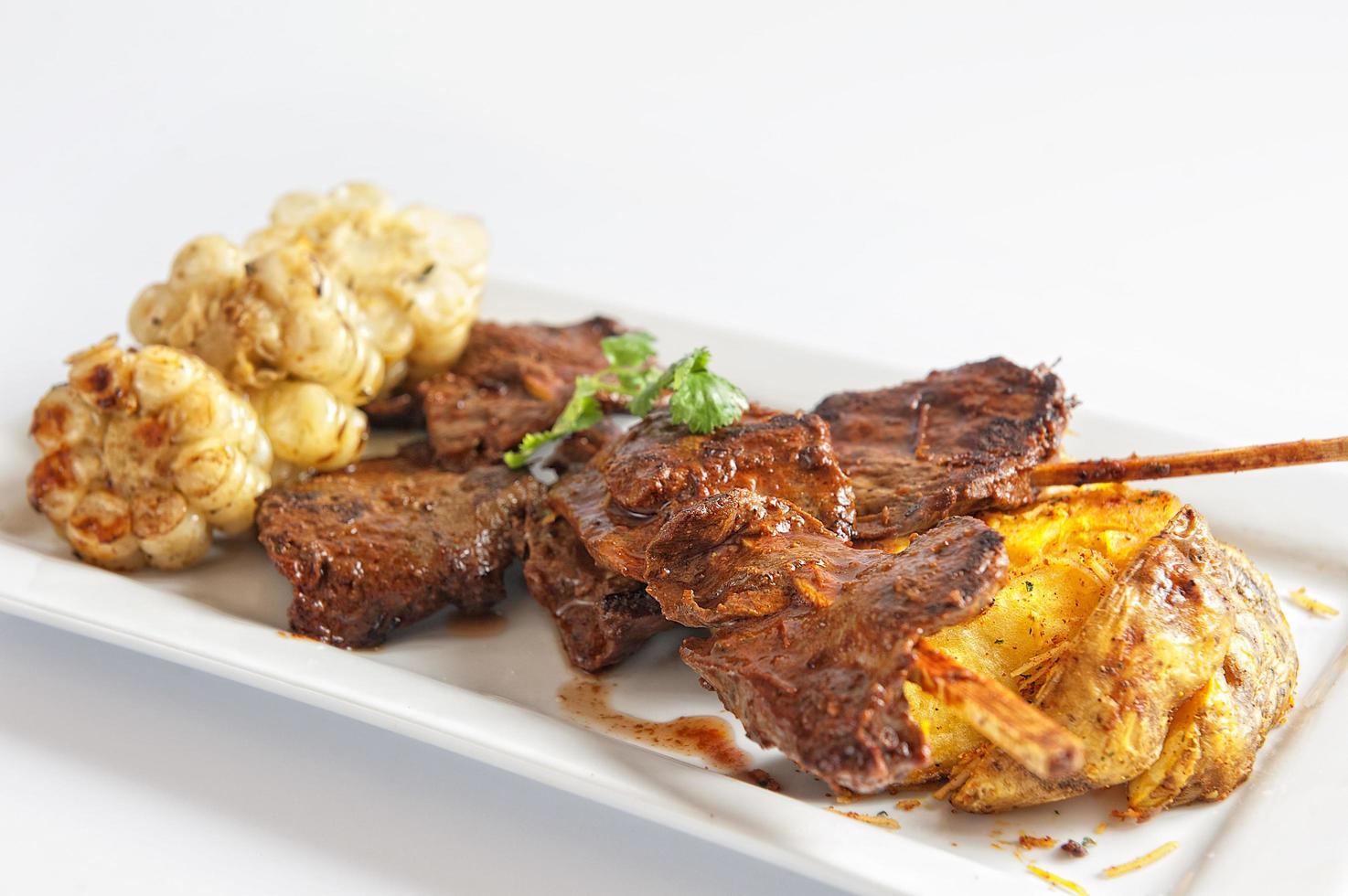 Grilled skewered beef heart meat with boiled potato and white corn photo