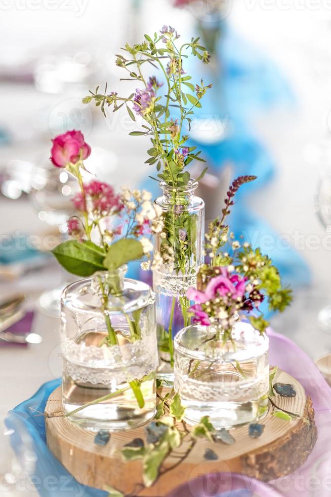 Decoración floral borrosa muy brillante con rosas rosadas gypsophila y jarrones de vidrio en un disco de madera foto