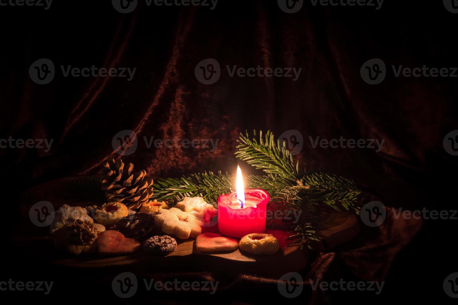 Vela roja encendida se encuentra entre las galletas navideñas decoradas sobre una tabla de madera foto