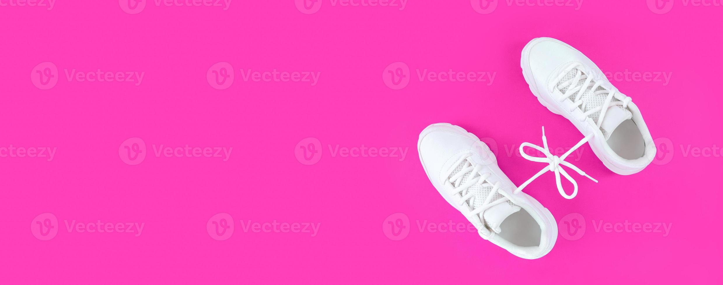 Pair of white sport shoes connected with laces bow on pink background Simple flat lay with copy space photo