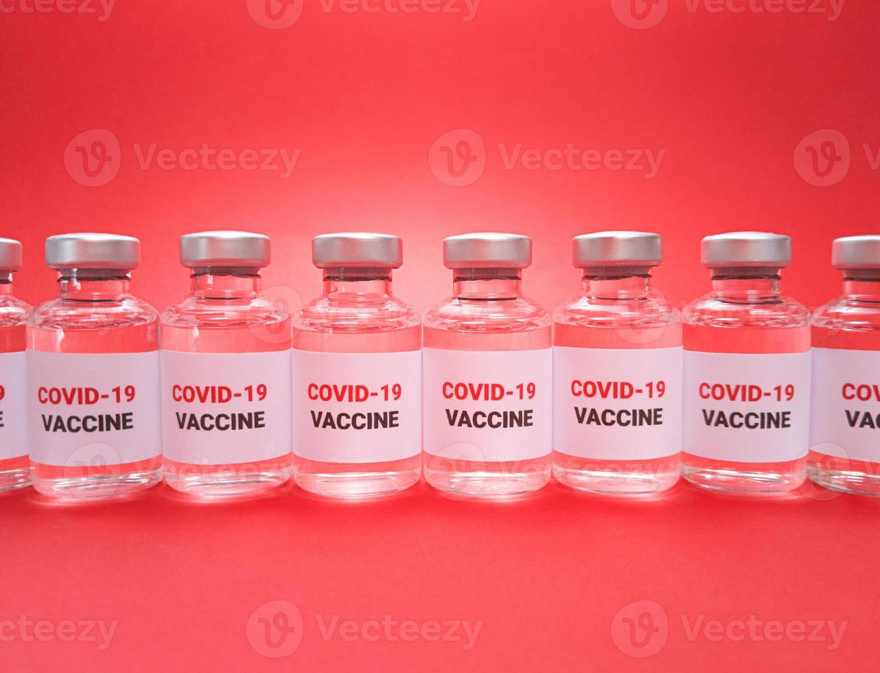 Many vials with covid 19 vaccine in a row on red background photo