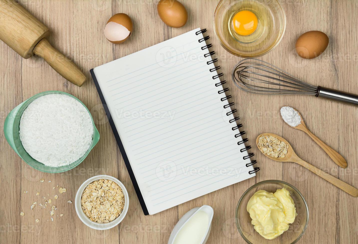 Vista superior de herramientas e ingredientes para hornear pasteles y cuaderno en blanco sobre fondo de madera foto