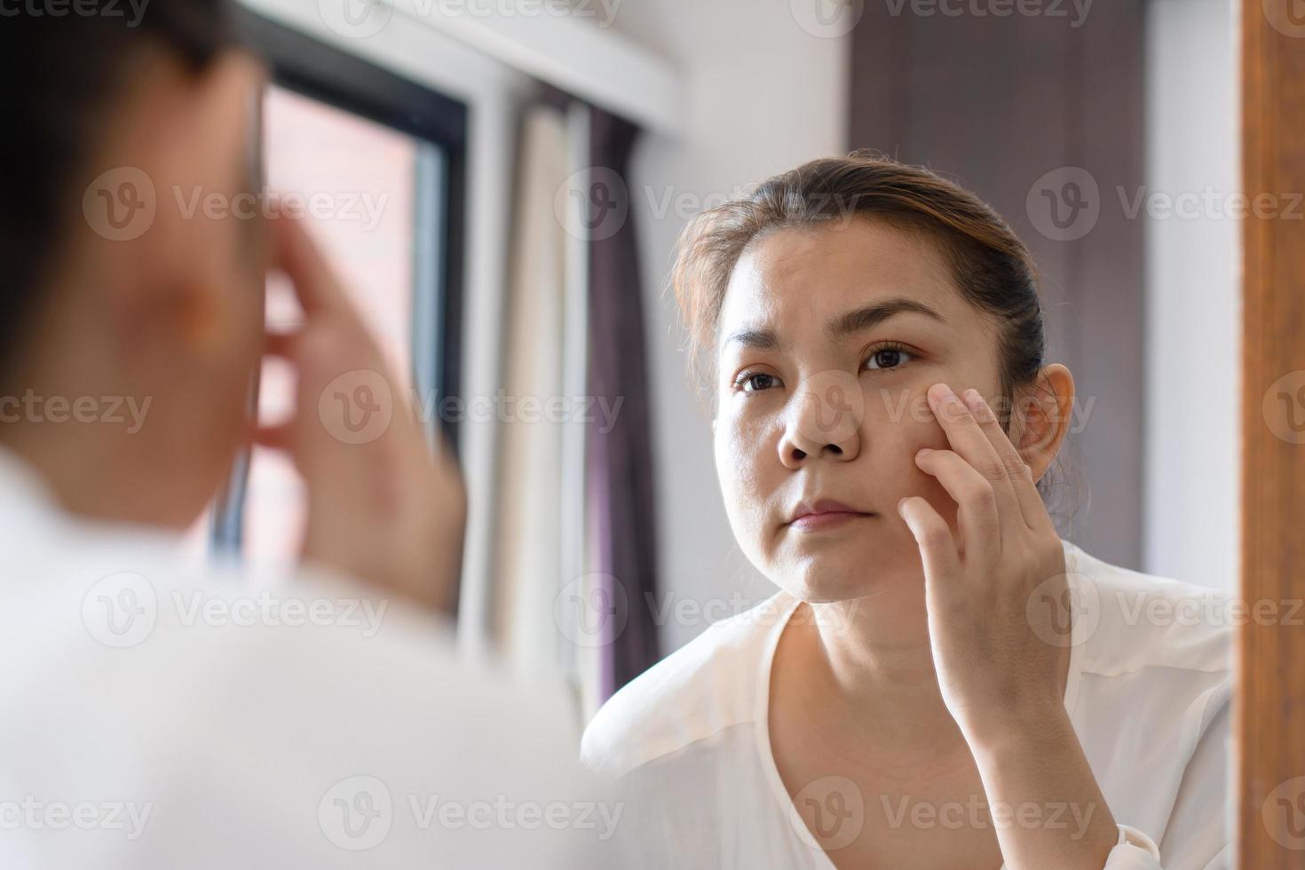 Mujer asiática de mediana edad mirando las arrugas en el espejo foto